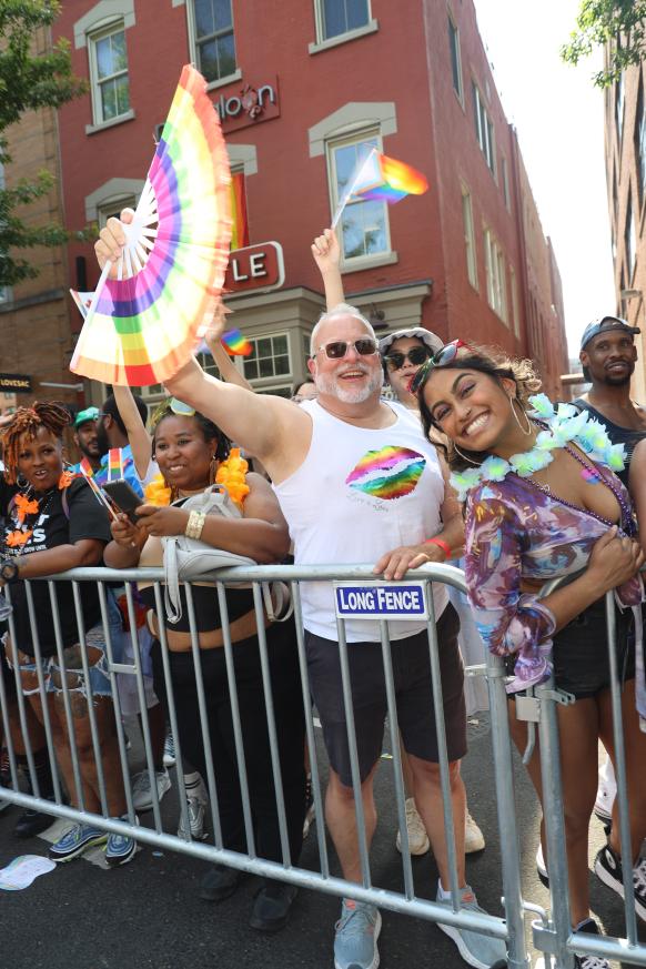 A man in a white tank top holding a rainbow fan.