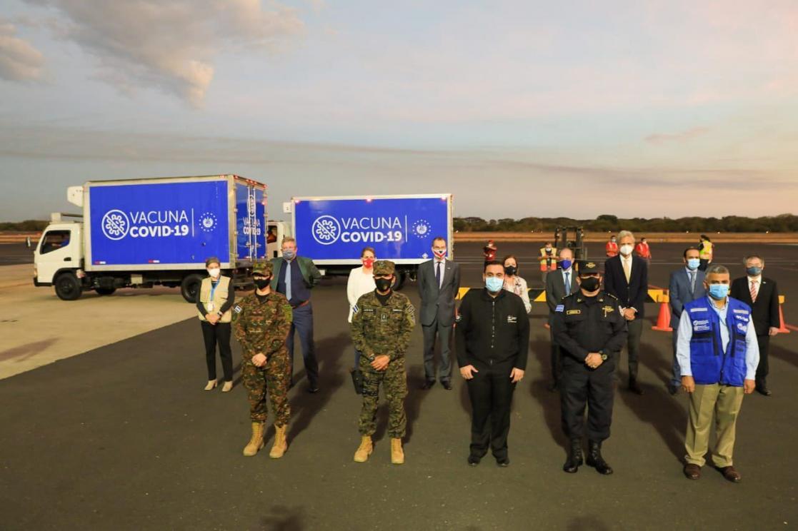 Group of people uniform on a runway with two trucks of vaccine COVID-19