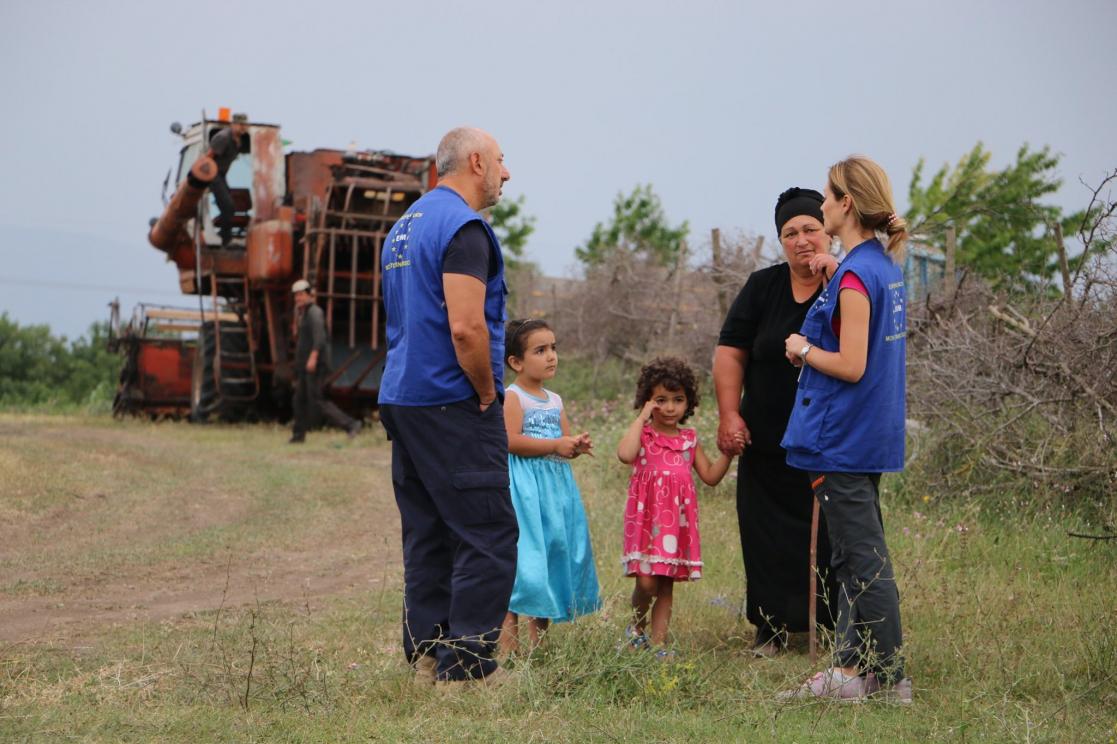 Man and woman in blue waistcoats talking to woman with two girls