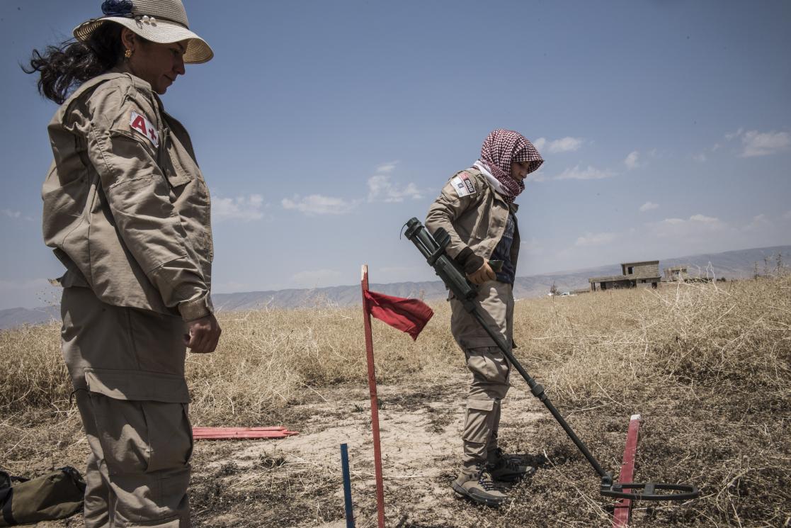 Two women in uniform using a metal detector on the floor