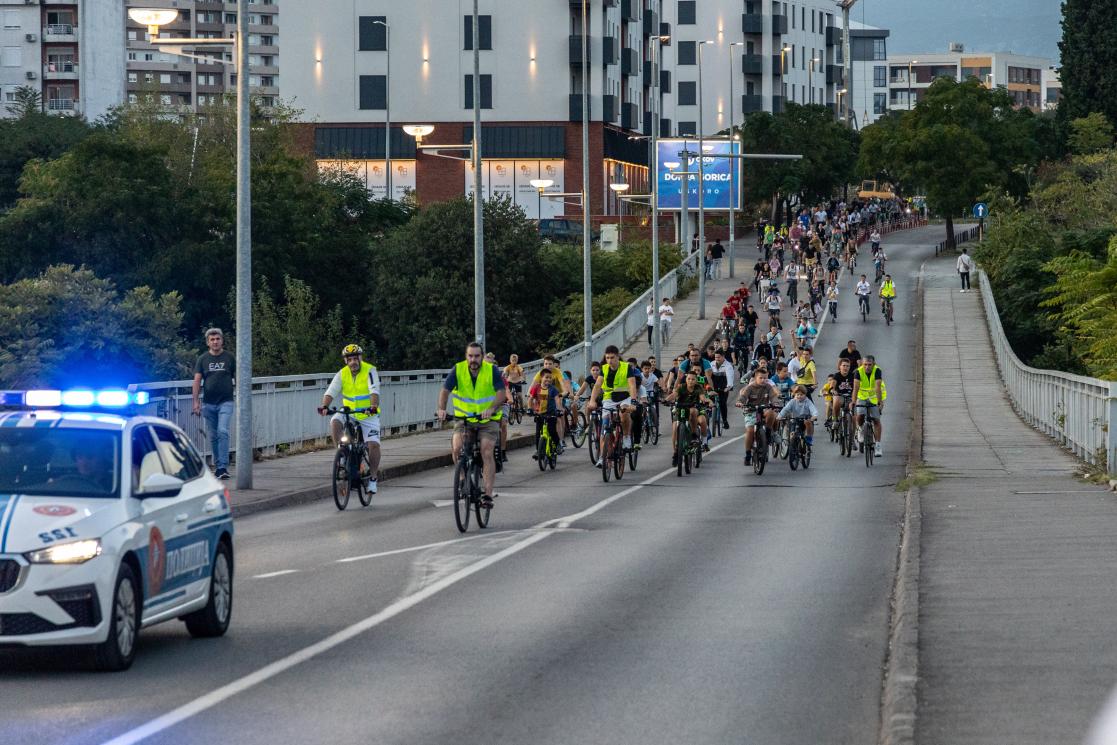 Police vehicle leading a group of people on bikes across the bridge. 