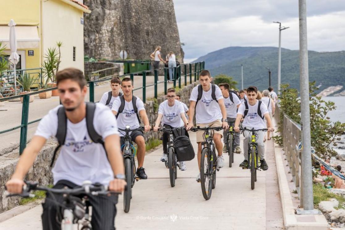 Students wearing white t-shirts riding bikes through Herceg Novi