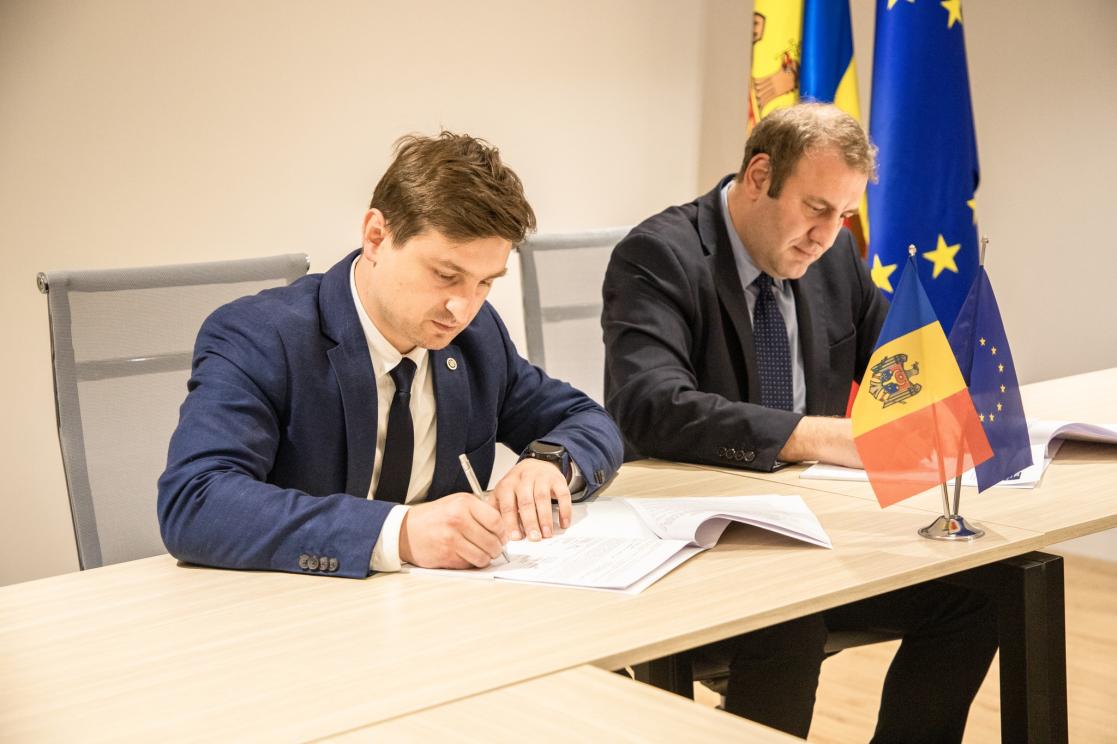 Two men at a signing ceremony with EU/Moldova flag in background.