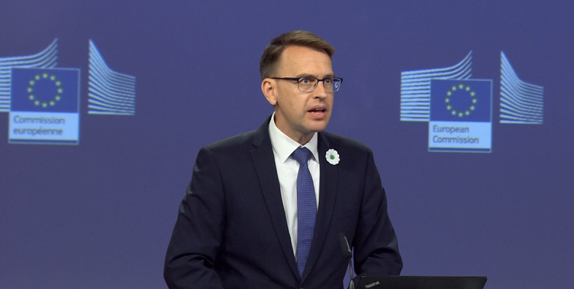 Man wearing a commemorative flower speaking from a dais.