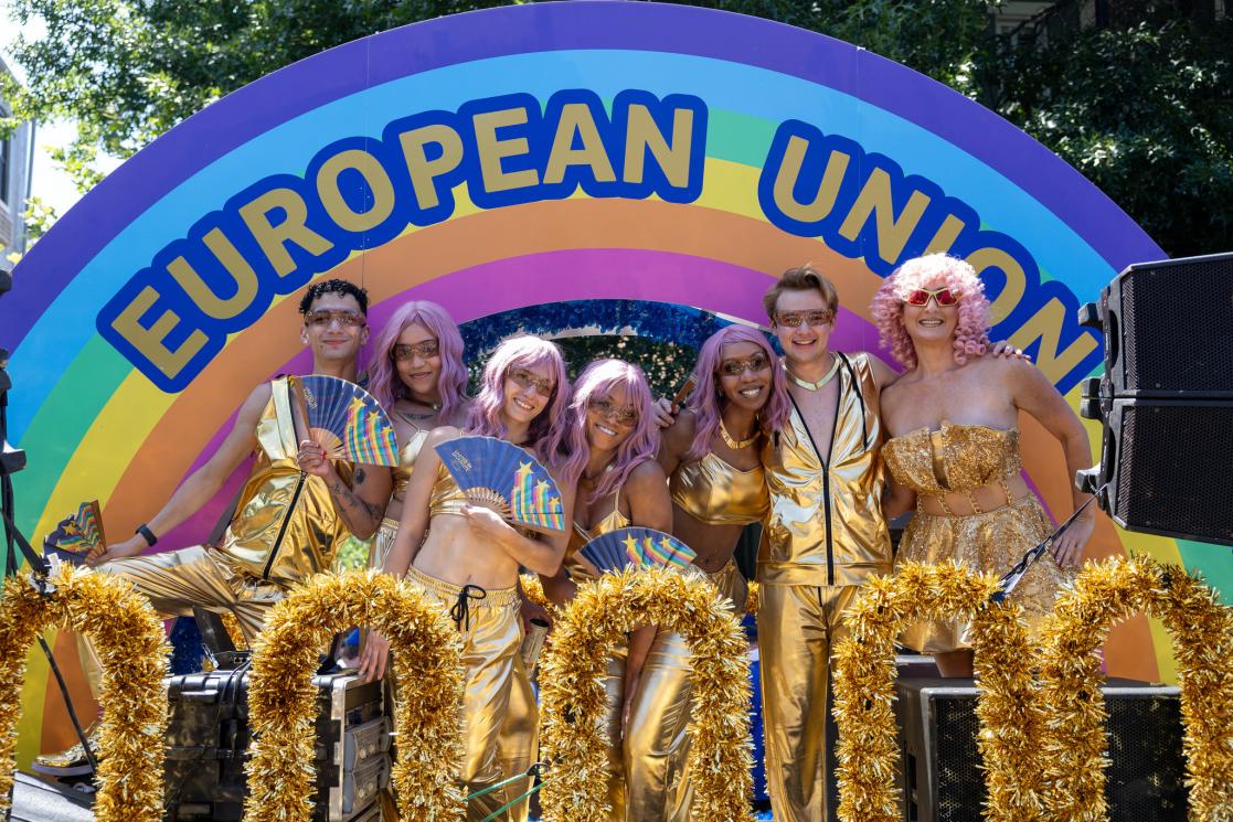 A group of dancers wearing gold outfits and pink wigs pose on a parade float.