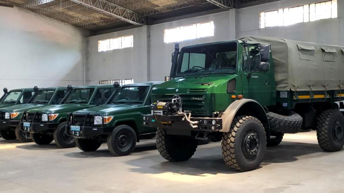 A line of new military vehicles & trucks in a storage facility.