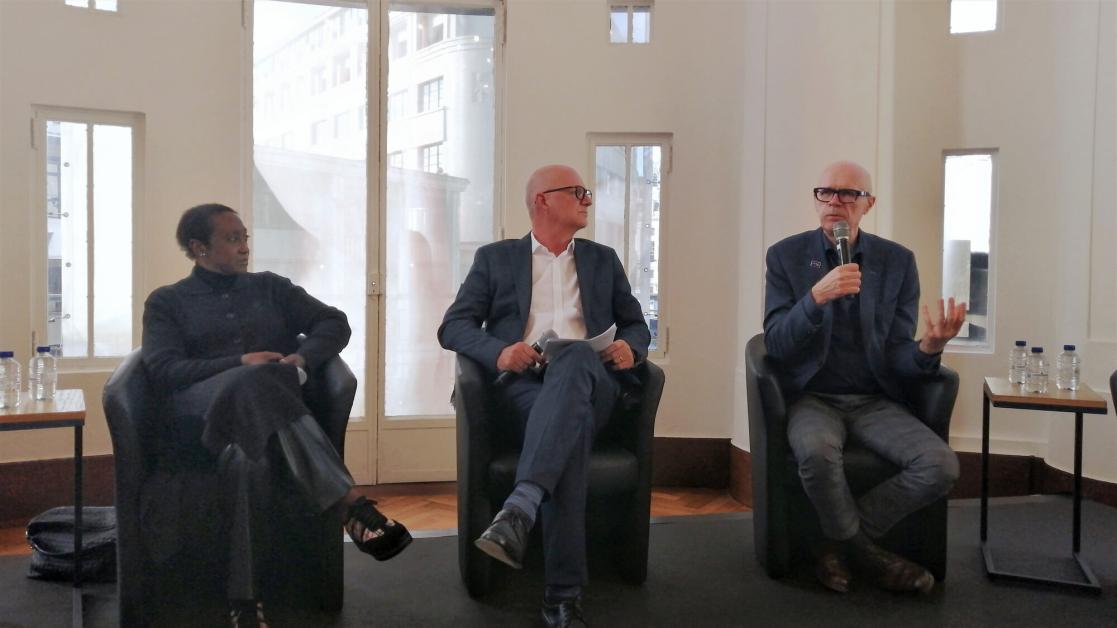 A woman and two men on the dais at a panel discussion.