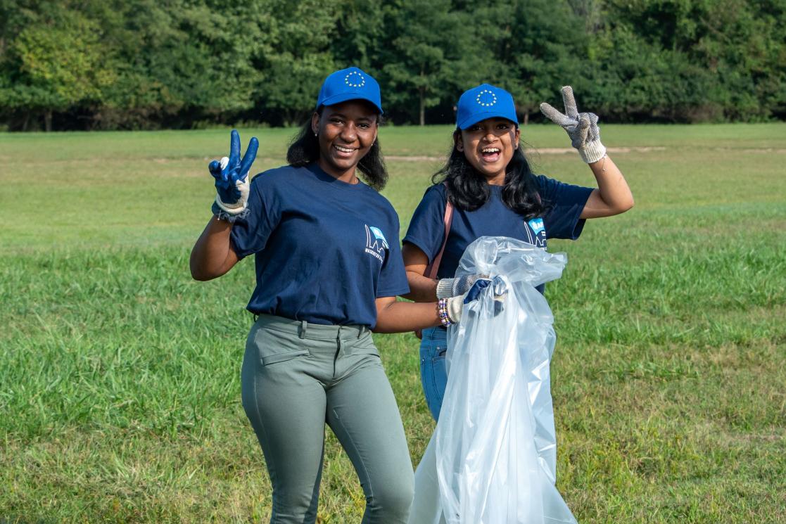 Two girls wearing EU hats and holding trash bags pose for the camera.