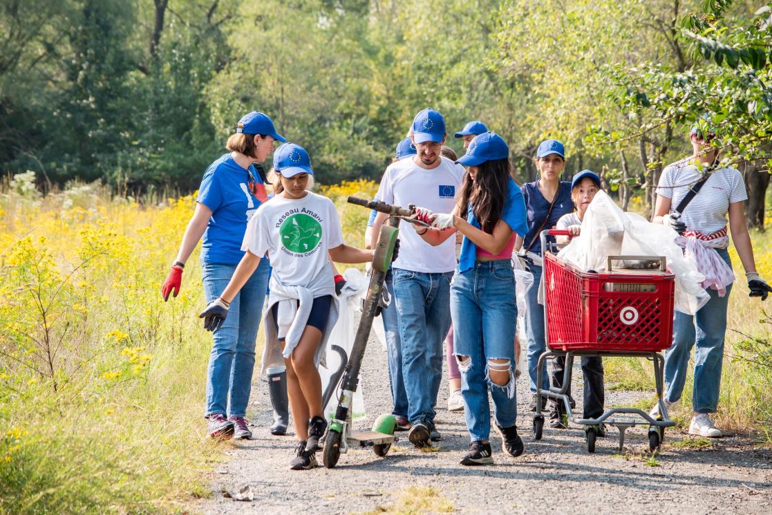 A group of volunteers in EU shirts and hats carry trash through a park.