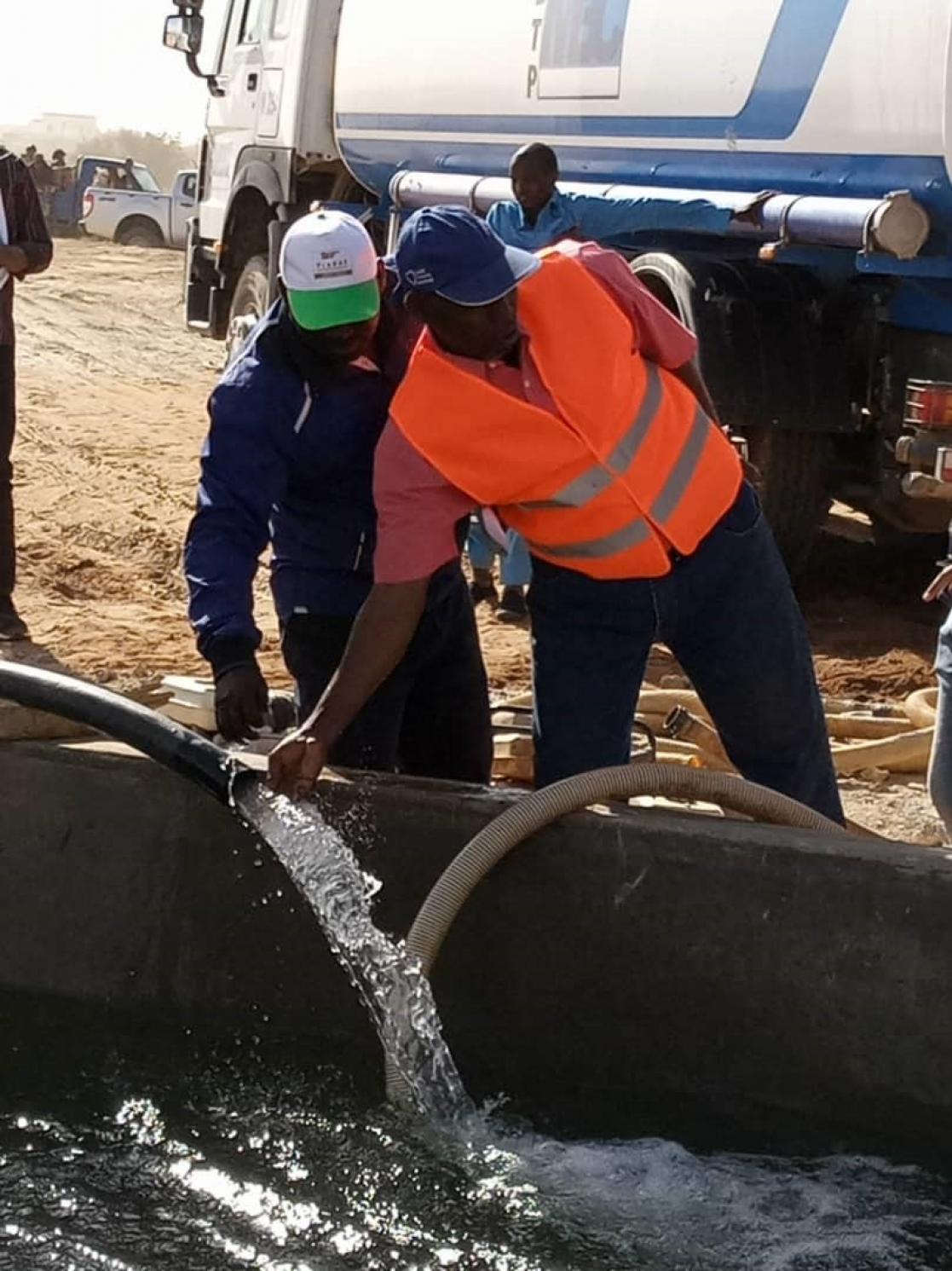 Two men looking at the water coming out of a water pipe