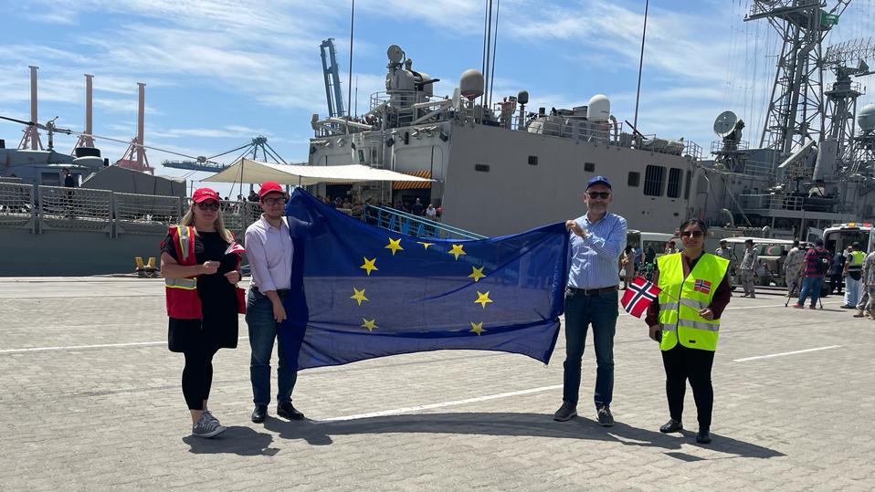 People hold EU flag with naval ship in background