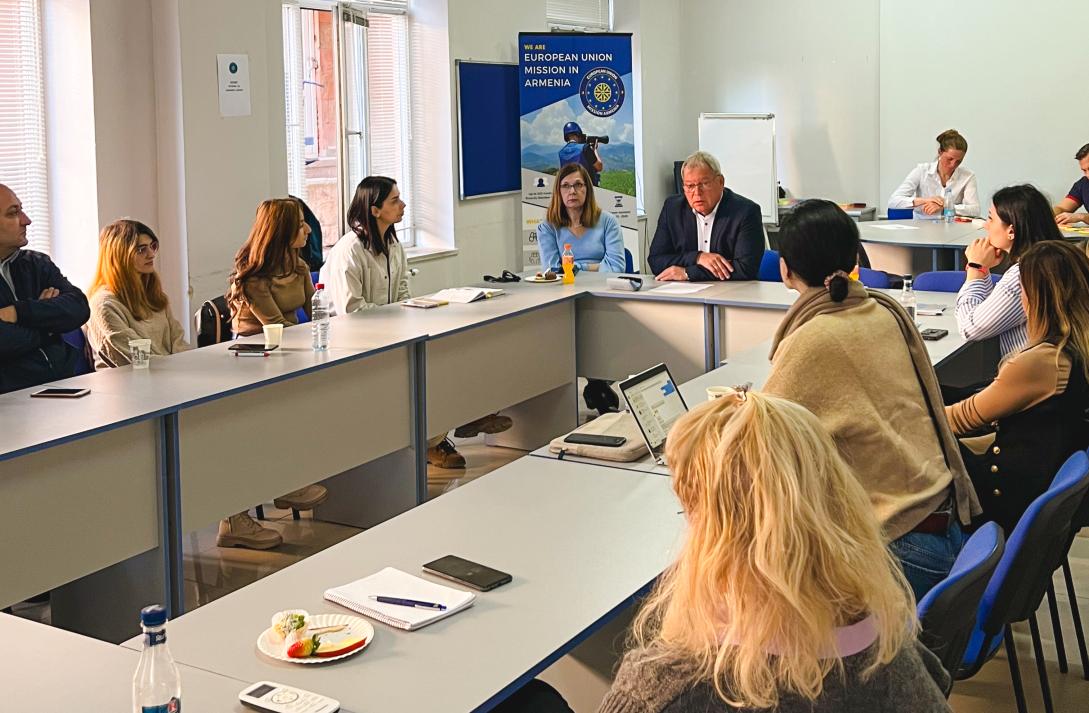 A group of 12 people in a meeting with the EUMA mission banner in the background.