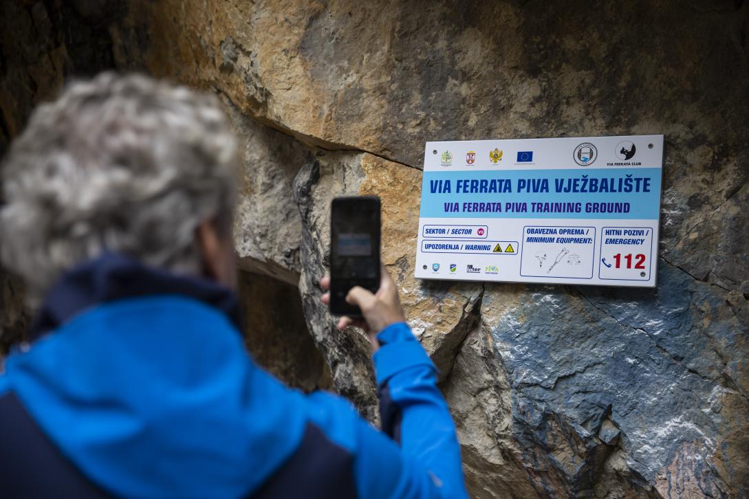 Ambassador Sattler taking picture of the sign for Via Ferrata mounted on the cliff