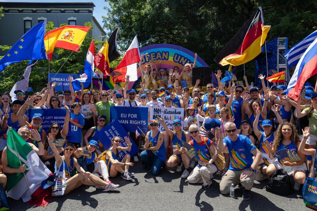 A large group of people pose in front of a colorful parade float while waving country flags.