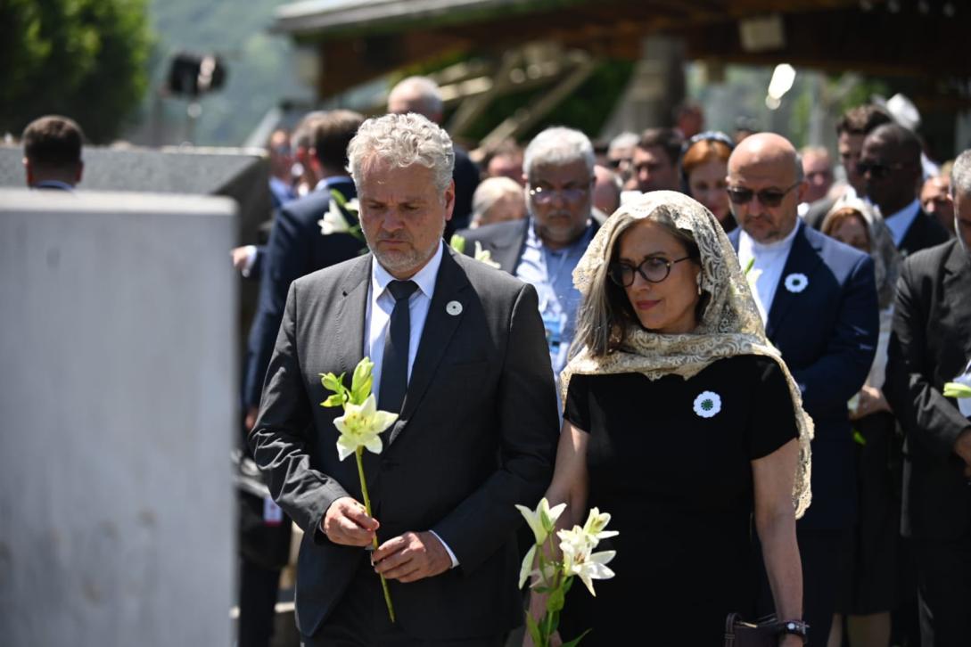 A man and a womon at a commemoration ceremony in solemn pose. 