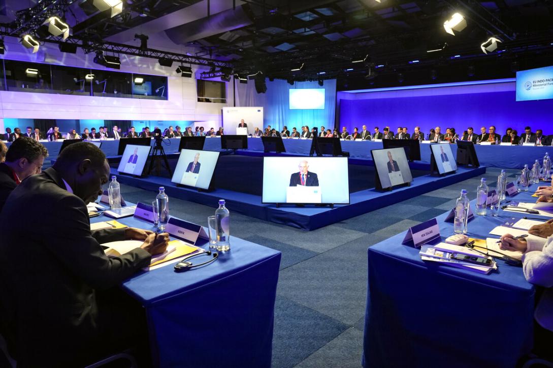 A VIP addresses a forum while appearing on several screens.