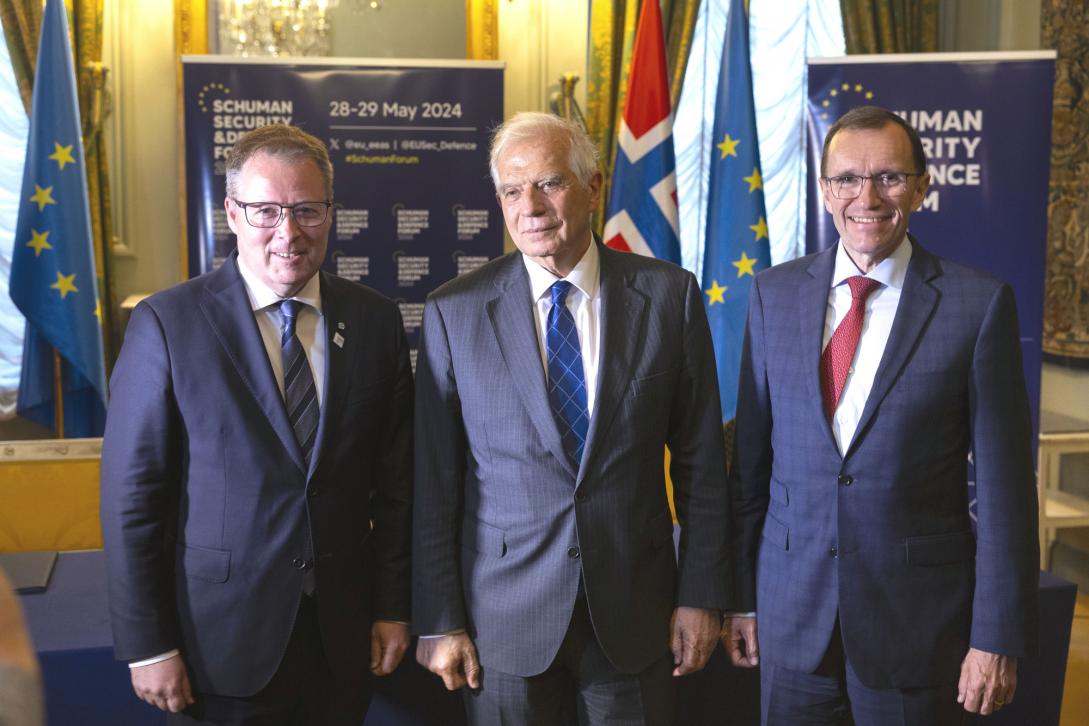 Three men pose in front of Schuman Forum posters