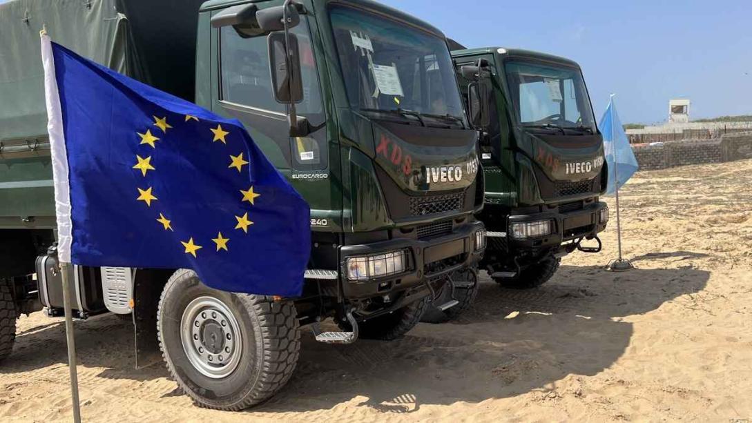 European flag foreground, two army trucks in background.