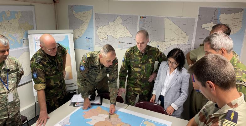 Military conference around a map with seven uniformed military and one civilian