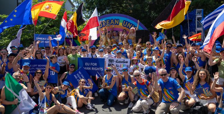 A large group of people pose in front of a colorful parade float while waving country flags.